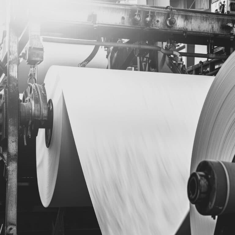 Massive rolls of pristine white paper ready for use in a busy print production warehouse. Giant paper rolls waiting to be transformed in an industrial print shop.